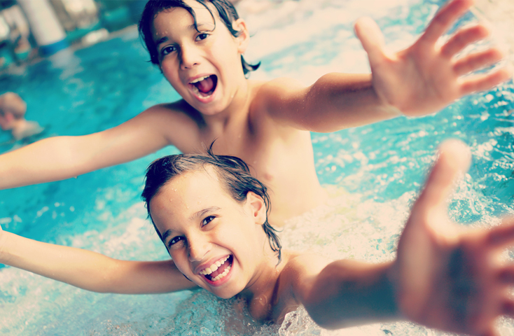 2 children in a pool smiling with their arms out stretched