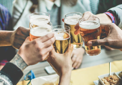 Multiracial group of friends enjoying a beer - Young people hands toasting and cheering aperitif beers half pint - Friendship and youth concept - Warm vintage filter - Focus on bottom hand