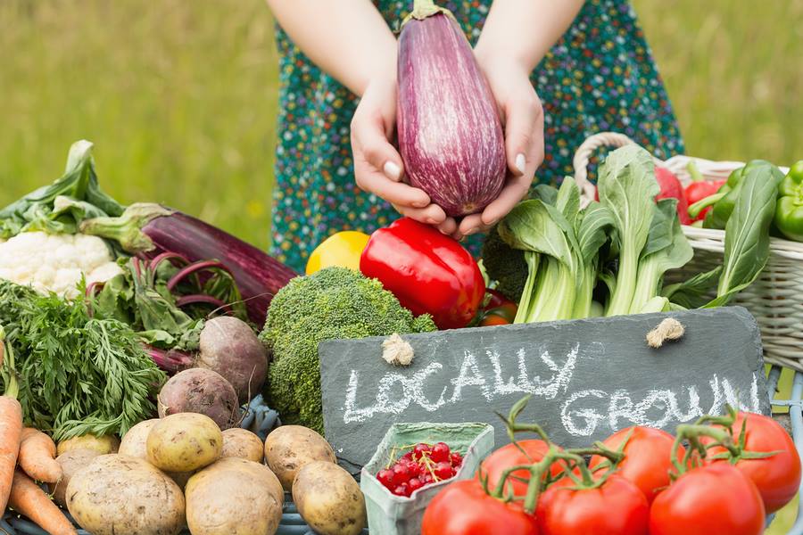women holding an eggplant with other locally grown produce around a table